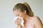 Young woman sneezing into tissue