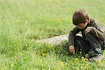 Boy crouching in grass, looking at something on the ground