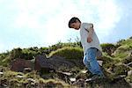 Boy standing on rocky hillside, low angle view