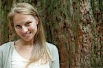 Young woman leaning against tree trunk, portrait