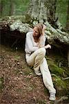 Woman sitting at base of tree in woods