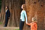 Mother and daughter leaning against tree, father standing separate in background