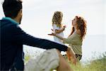 Mother talking with young daughter outdoors, father watching from foreground