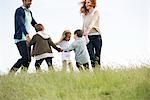 Family playing ring-around-the-rosy in meadow