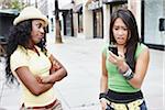 Woman with Cell Phone Looking Surprised While Friend Looks on Disapprovingly