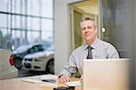 Car salesman sitting at desk in showroom