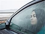 Teenage girl looking out wet car window