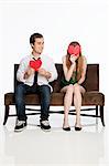 Young couple sitting on sofa with heart shapes against white background