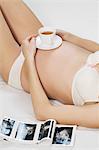 Mid section of pregnant woman lying in bed with tea cup and pregnancy report