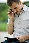 Man using cell phone and digital tablet outdoors