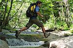 Man jumping over stream through woods