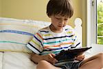 Boy sitting on bed, using digital tablet