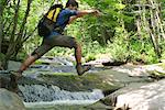 Man jumping over stream through woods