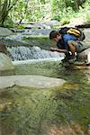 Man crouching by stream, catching water in cupped hands