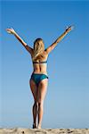 Woman at the beach with arms raised in air, rear view