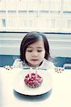 Kleines Mädchen bläst Kerzen auf Geburtstagskuchen