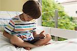 Boy sitting on bed, using digital tablet