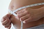 Pregnant woman measuring her belly with measuring tape, cropped