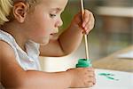 Little girl dipping paintbrush into paint