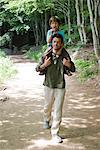 Father carrying son on shoulders, walking in woods