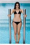 Young woman on swimming pool ladder leaning back over water