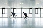 One businessman riding bicycle, the other skateboarding