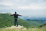 Man standing on top of rock with arms outstretched, rear view