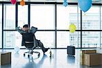 Businessman sitting in new office with balloons and boxes