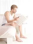 Young man reading newspaper in bed