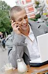 Jeune homme à l'aide d'ordinateur portable et téléphone portable dans un café en plein air