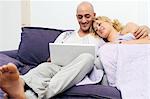 Happy couple on couch using laptop