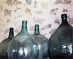 Four round glass bottles in front of stone wall