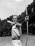 1930s GIRL WEARING A CAMP JUMPER WITH WIDE LEATHER BELT ABOUT TO RELEASE AN ARROW FROM BOW