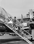 1950s FAMILY FATHER MOTHER DAUGHTER SON BOARDING PROPELLER AIRLINER BY CLIMBING GANGWAY STAIRS AT AIRPORT