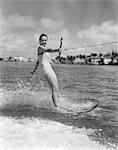 1950s SMILING WOMAN IN BATHING SUIT WATER SKIING WAVING ONE HAND