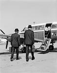 1960s TWO BUSINESSMEN WALKING TOGETHER TO A SMALL PRIVATE PROPELLER AIRPLANE CARRYING BRIEFCASE