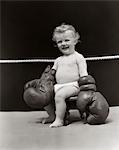 1930s SMILING BABY SEATED ON STOOL IN BOXING RING WEARING OVERSIZED BOXING GLOVES WEARING DIAPER