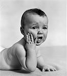 1940s BABY LYING ON STOMACH WITH HAND ON CHEEK & DISTRESSED LOOK ON FACE