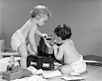 1960s PAIR OF BABIES AROUND ADDING MACHINE WITH TELEPHONE OFF HOOK & PAPERS SCATTERED ON FLOOR