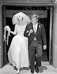 1960s COUPLE BRIDE AND GROOM ARM IN ARM LEAVING CHURCH UNDER SHOWER OF RICE