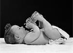 1950s BABY LYING ON BACK DRINKING FROM BOTTLE HELD BY FEET & HANDS