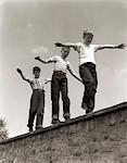 ANNÉES 1950 TROIS GARÇONS RIANTES MARCHE AU SOMMET DU MUR DE PIERRE BRAS TENDUS ÉQUILIBRAGE JEU SUIVRE LE LEADER