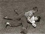 1950s TWO BOYS WEAR TEE SHIRTS BLUE JEANS PLAYING ROUGH FIGHTING WRESTLING ON THE GRASS