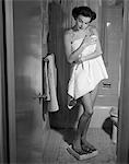 1950s WOMAN WRAPPED IN TOWEL STEPPING ON BATHROOM SCALE