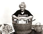 1920s - 1930s - 1940s SENIOR WOMAN WASHING CLOTHES IN OLD FASHIONED WOODEN TUB AND WASHBOARD