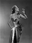 1950s WOMAN WEARING METALLIC EVENING GOWN HOLDING UP WINE GLASS PROFILE INDOOR