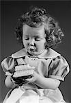 1940s LITTLE GIRL EATING PIECE OF CAKE WITH CHOCOLATE ICING