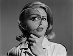 1960s BLOND WOMAN MAGNIFYING GLASS HELD UP TO AND ENLARGING ONE EYE