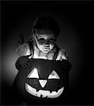 1950s LITTLE GIRL STANDING OVER CARVED PUMPKIN FACE LIT BY CANDLE