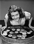 1940s SMILING TEEN GIRL LEANING OVER TUB ABOUT TO BEGIN BOBBING FOR APPLES FLOATING IN THE WATER